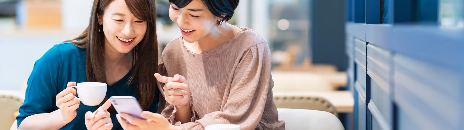 2人の女性がスマートフォンを見ながら、会話をしている画像